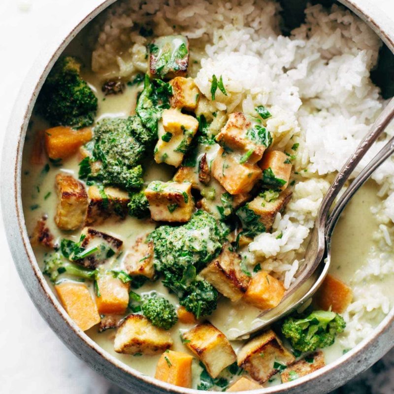 Utensils sit in a bowl of rice, vegetables and tofu.