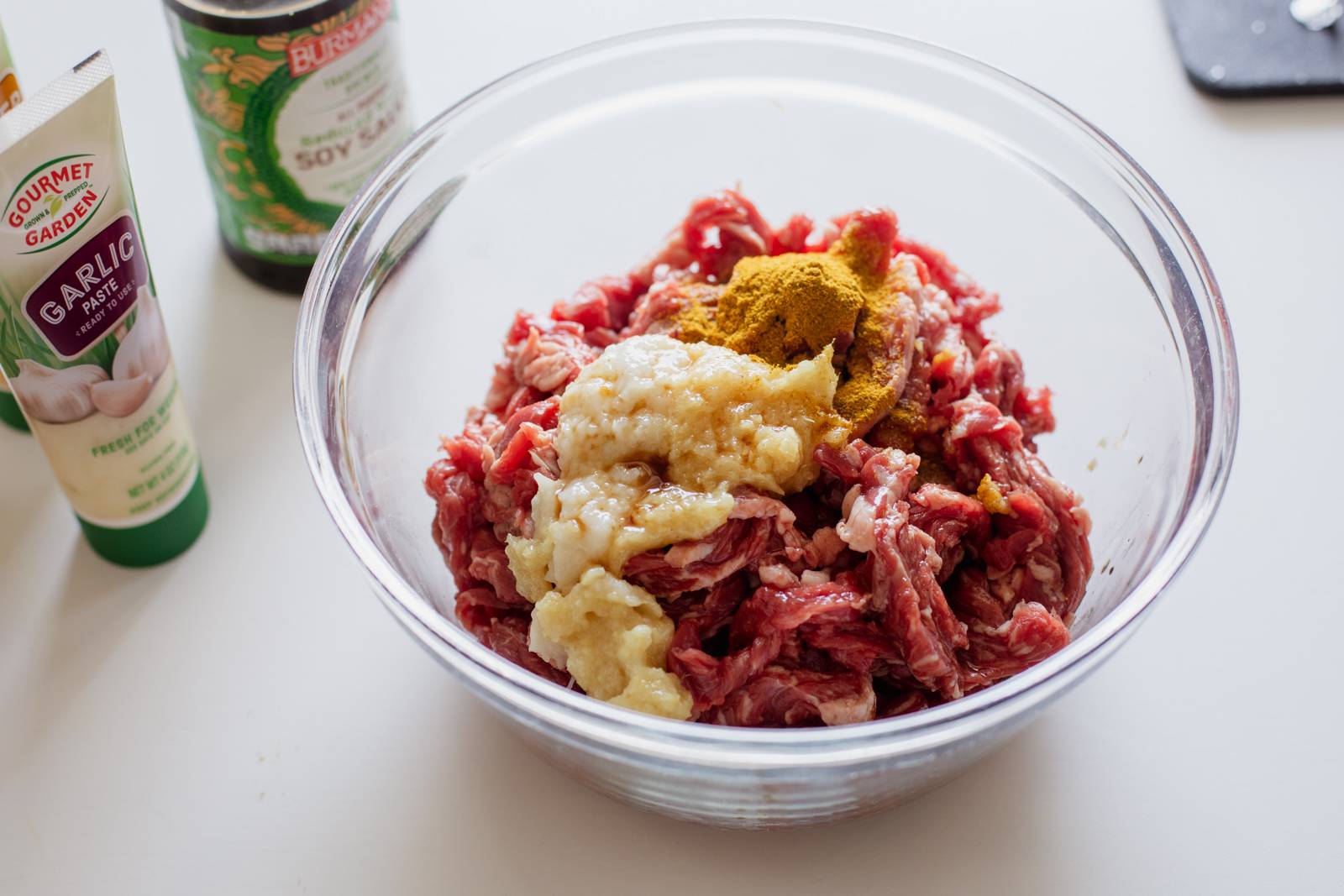 Thinly sliced skirt steak in a bowl with garlic, ginger, and curry powder.