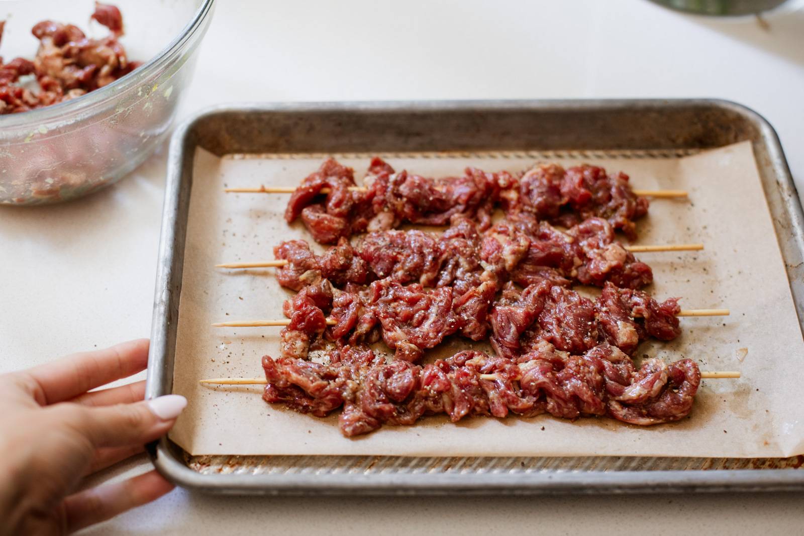 Thinly sliced steak on skewers on a sheet pan.