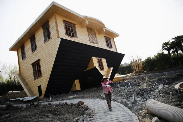 A laborer works at an upside-down house under construction at Fengjing Ancient Town, Jinshan District, south of Shanghai, March 17, 2014. Workers are putting the final touches on this eccentric tourist attraction built at the “China Folk Painting Village”. Furniture will also be placed upside down in the house, which is expected to open the public in April, according to local media. (Photo by Carlos Barria/Reuters)