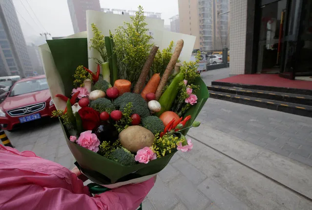 A woman receives a bouquet made of vegetables and flowers, priced at 238RMB, from a delivery staff of a florist outside an office building on Valentine's Day in Beijing, China, February 14, 2017. (Photo by Jason Lee/Reuters)