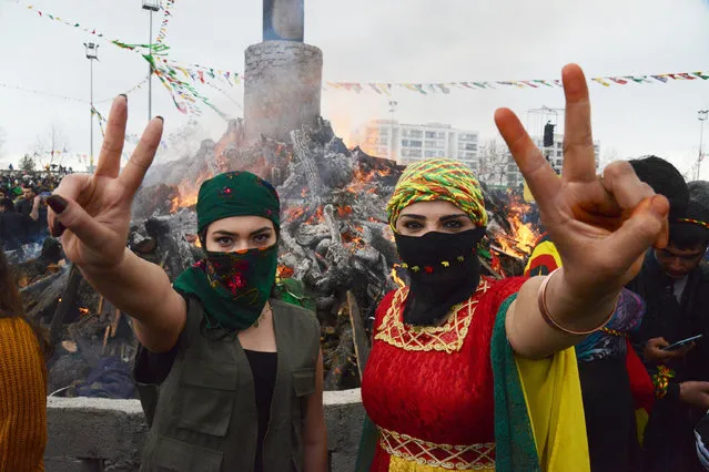 Young women flash the victory sign in front of a bonfire as Turkish Kurds gather during Newroz celebrations for the new year in Diyarbakir, southeastern Turkey, on March 21, 2017. Newroz (also known as Nawroz or Nowruz) is an ancient Persian festival, which is also celebrated by Kurdish people, marking the first day of spring, which falls on March 21. (Photo by Ilyas Akengin/AFP Photo)