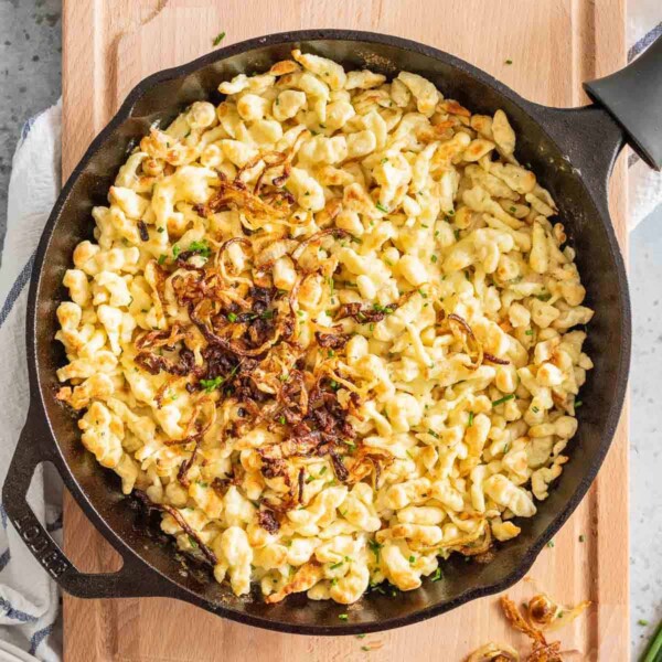 Käsespätzle in a cast iron pan on a wooden board.