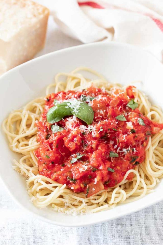 A white plate, with spaghetti topped with tomato sauce, garnished with basil leaves and parmigiano.