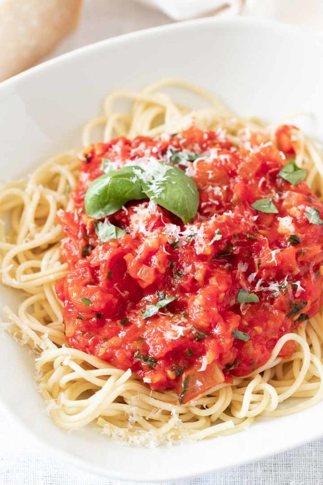 Close-up of a white plate of spaghetti topped with tomato sauce, basil leaves and Parmigiano.