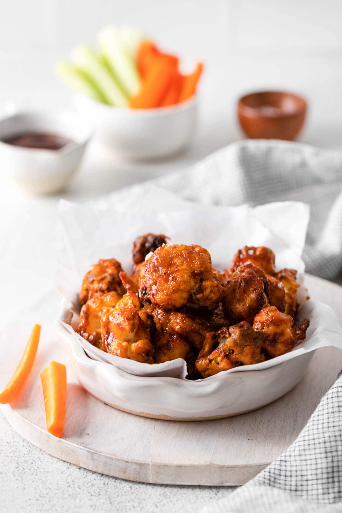 A wooden board with a bowl of cauliflower wings and some carrots.