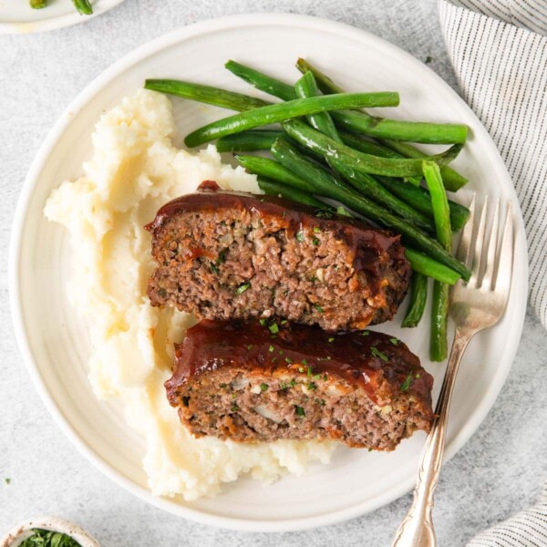 A plate with two slices of meatloaf, mashed potatoes, and green beans.