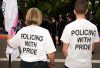 Two individuals stand together, wearing white shirts that read "Policing with Pride." They support LGBTQ+ inclusivity alongside police officers at a vibrant, community-oriented event.