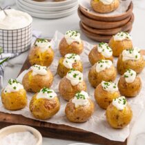 Mini baked potatoes topped with sour cream and chives on parchment paper.