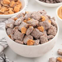 Butterfinger Puppy Chow in a white bowl with crushed Butterfinger pieces.