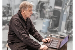 Old and experienced mechanic or technician sitting by his laptop in the auto repair shop studying with prodiags pre-learning training concept for car workshops and automotive garages.