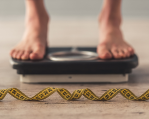 Cropped image of person's feet standing on a scale with a tape measure in the foreground. weight loss from Ozempic concept