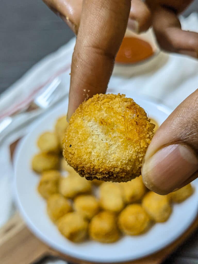 one popcorn chicken in focus done in air fryer with others blurred on a white plate 