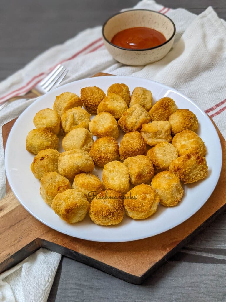 popcorn chicken done in air fryer on a white plate with ketchup in the background.