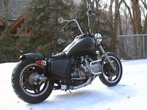 A stripped down bobber style build on a Honda GL1100 motorcycle. Featuring tall ape hanger bars with iron cross mirrors, a bullet tail light lens and comstar wheels.