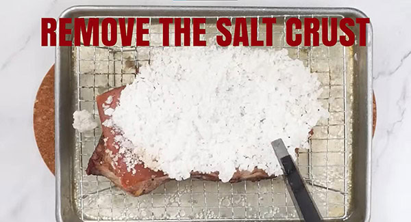 Salt crust on the pork belly is removed using tongs. 