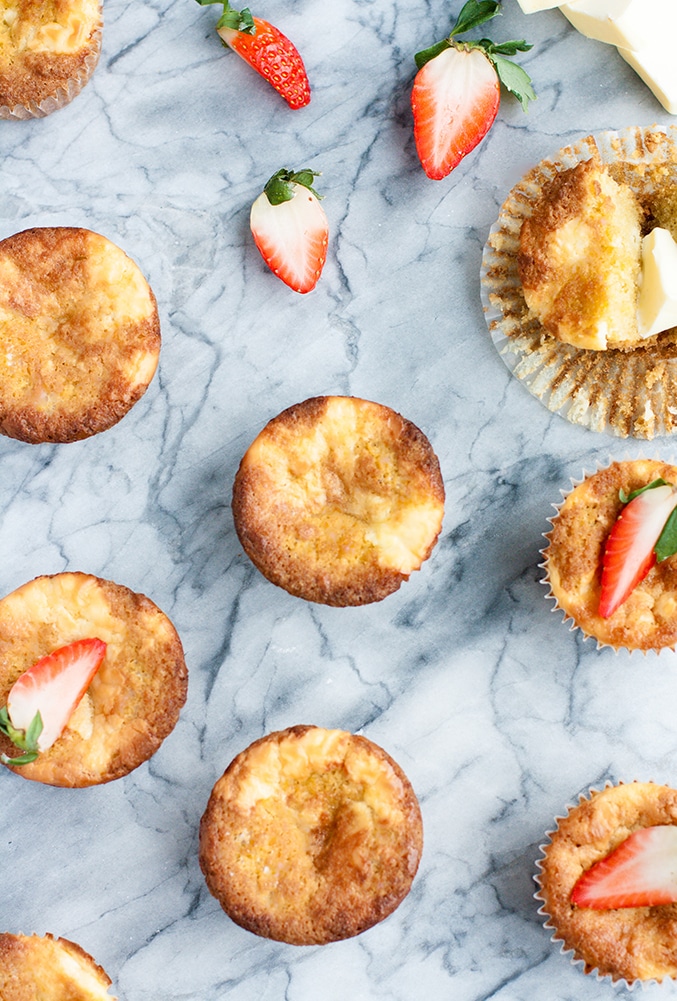 Strawberry Cream Cheese Muffins atop a marble kitchen counter surrounded by halved strawberries