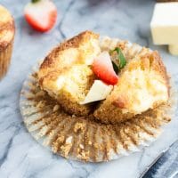 strawberry cream cheese muffin cut in half atop a marble kitchen counter with halved strawberries in the background