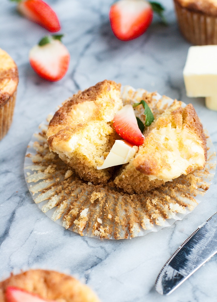 strawberry cream cheese muffin cut in half atop a marble kitchen counter with halved strawberries in the background