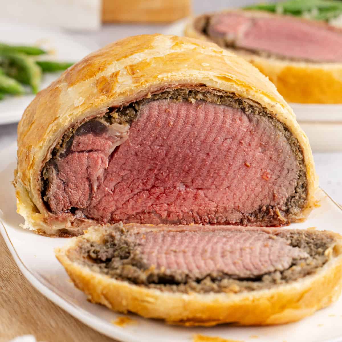 square image of a beef wellington with a slice cut from the end to show the roast and layers inside