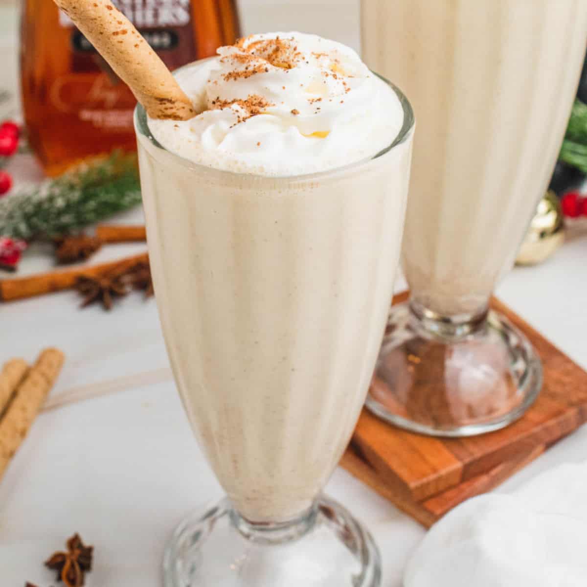 square image of a boozy eggnog milkshake topped with whipped crema and nutmeg