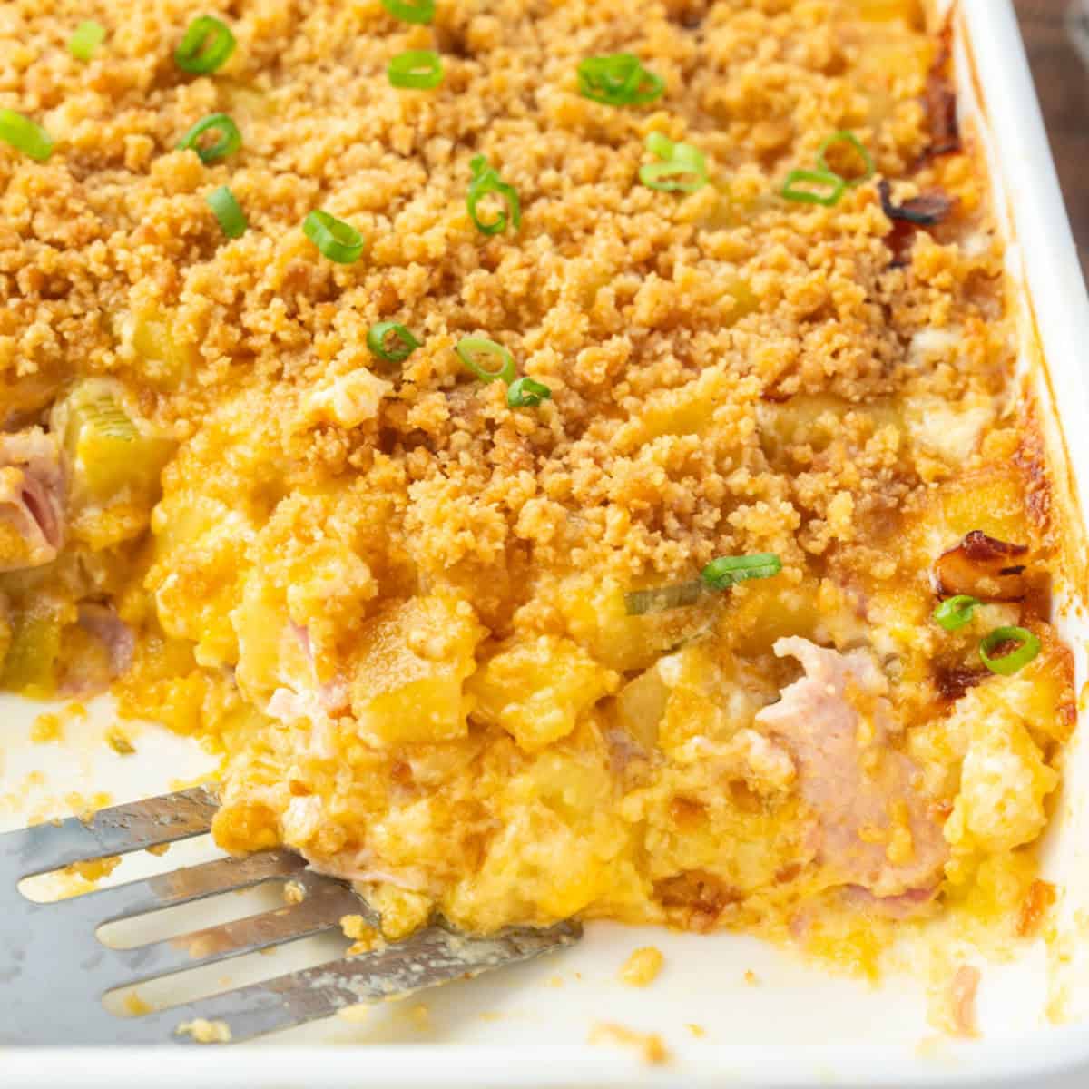 square image of a spatula in a dish of cheesy ham and hashbrown casserole