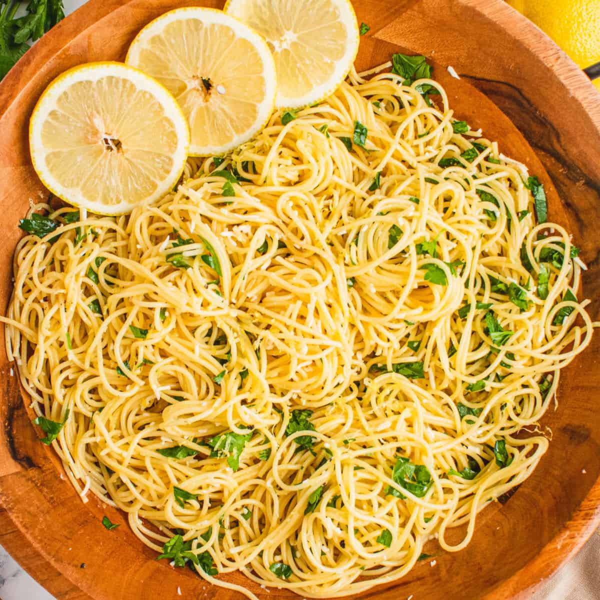 square image of lemon spaghetti in a wooden serving bowl with lemon slices