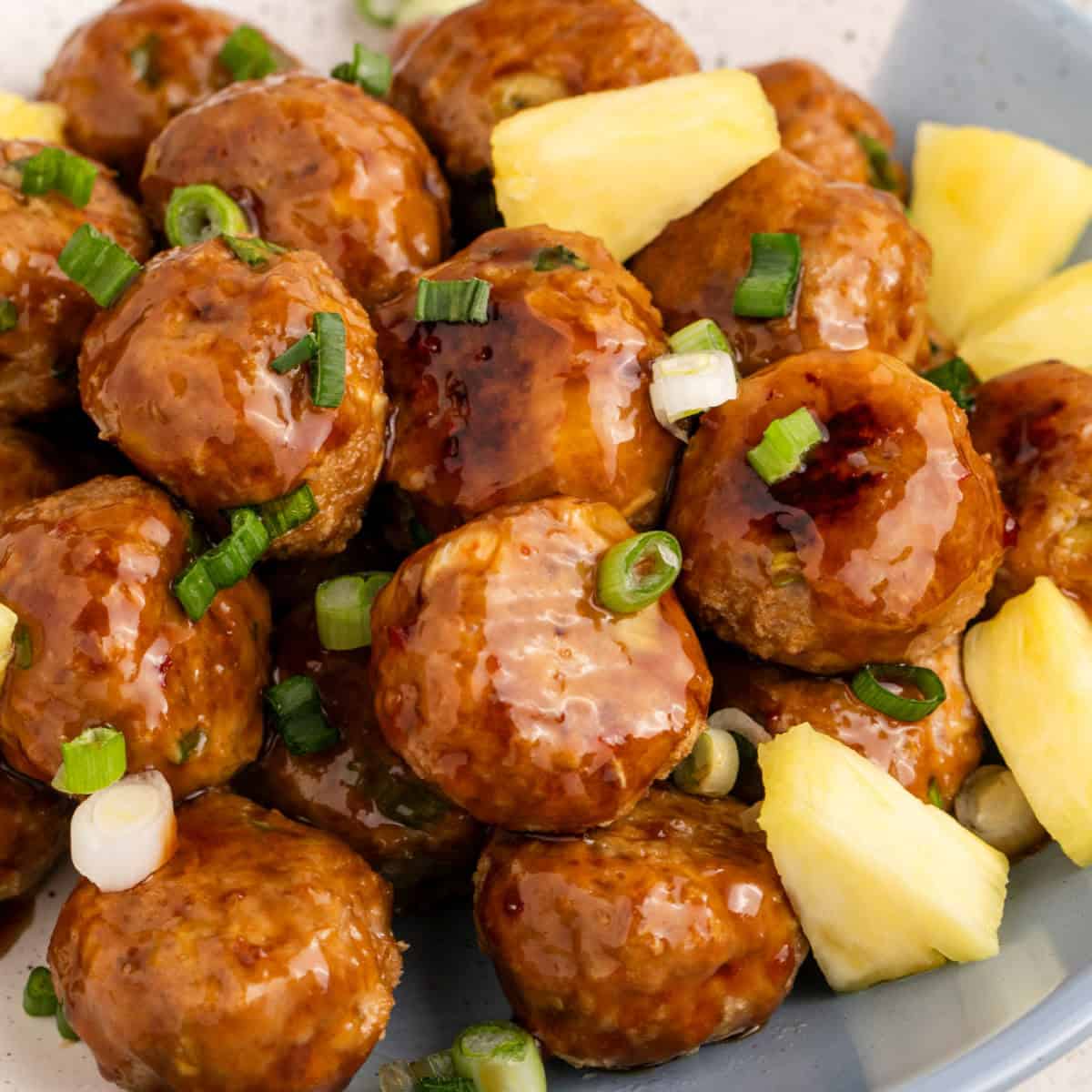 square image of pineapple teriyaki turkey meatballs in a serving bowl with green onion and pineapple for garnish