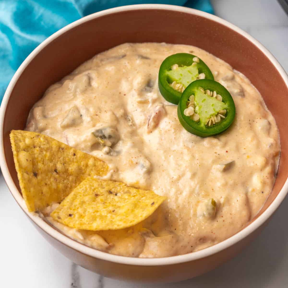 square image of a bowl of slow cooker queso dip with jalapeno slice and tortilla chips