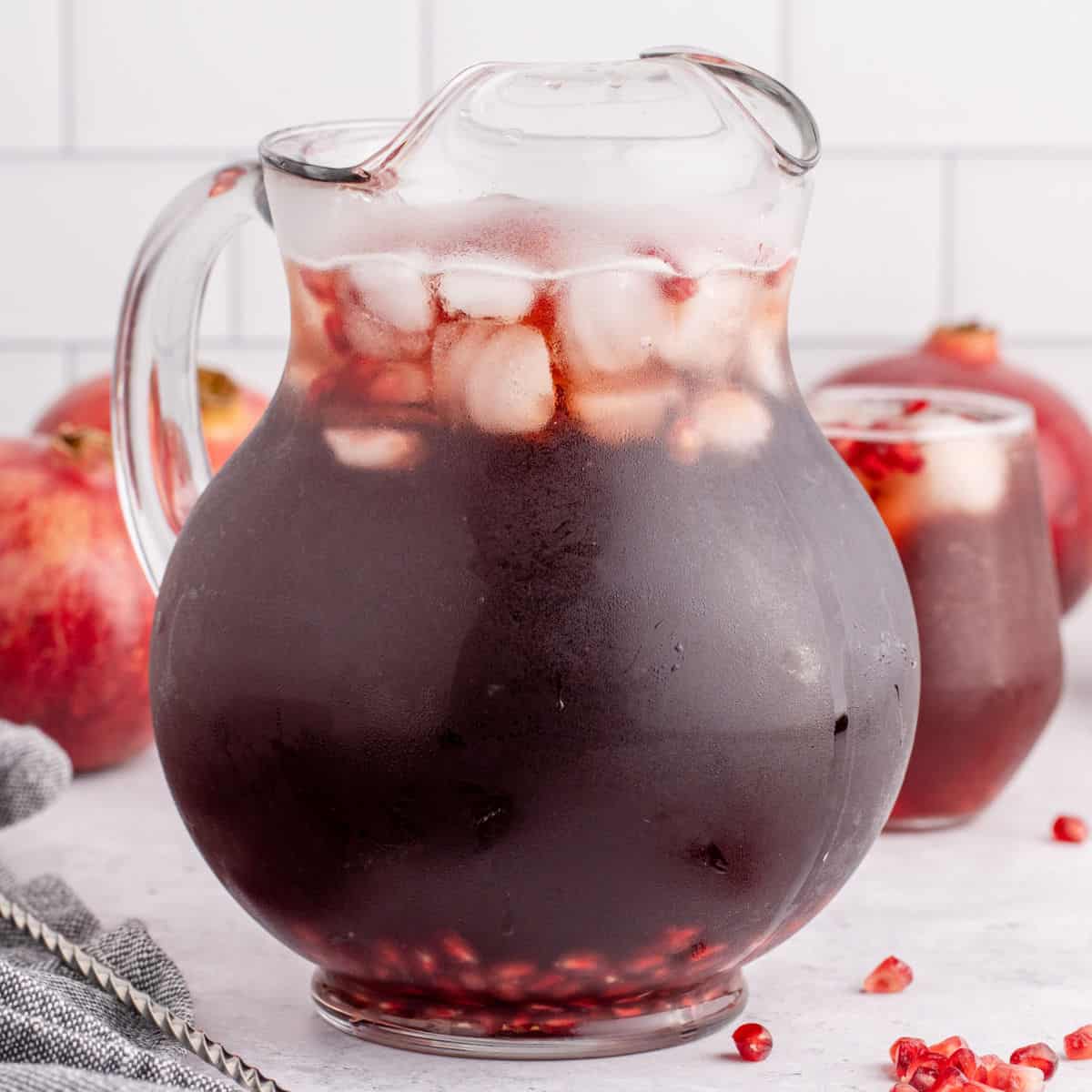 square image of spiked pomegranate punch in a pitcher with ice