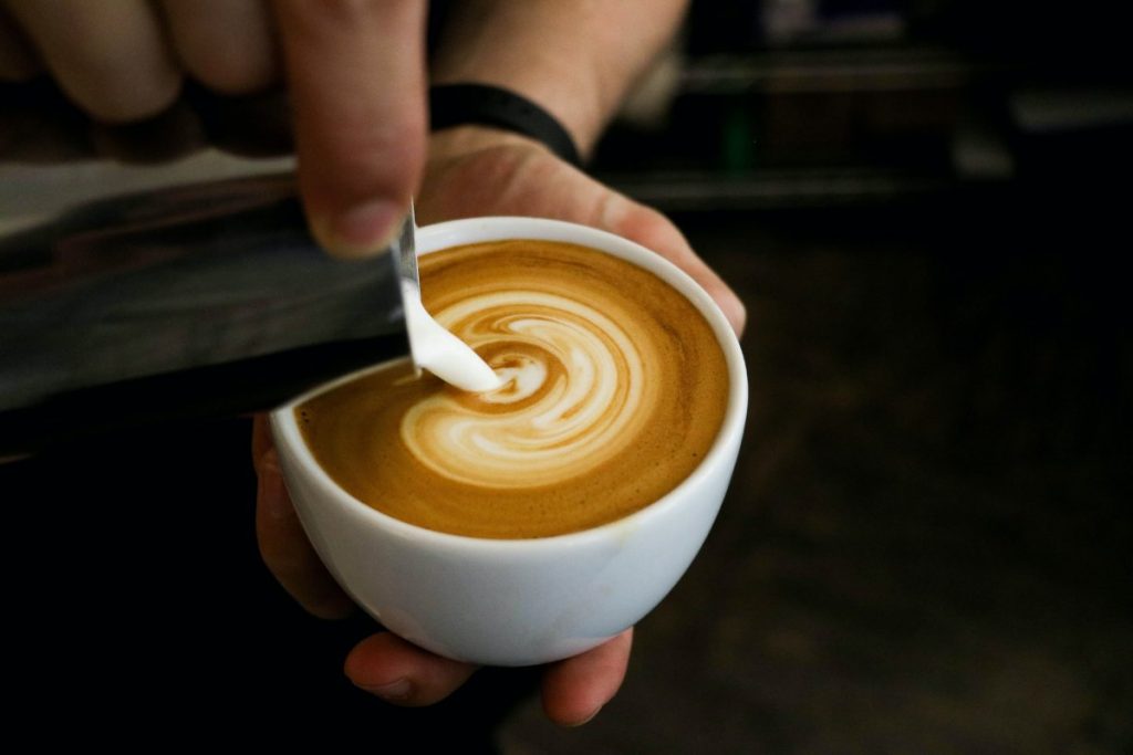 Person making latte, one of the many types of coffee drinks