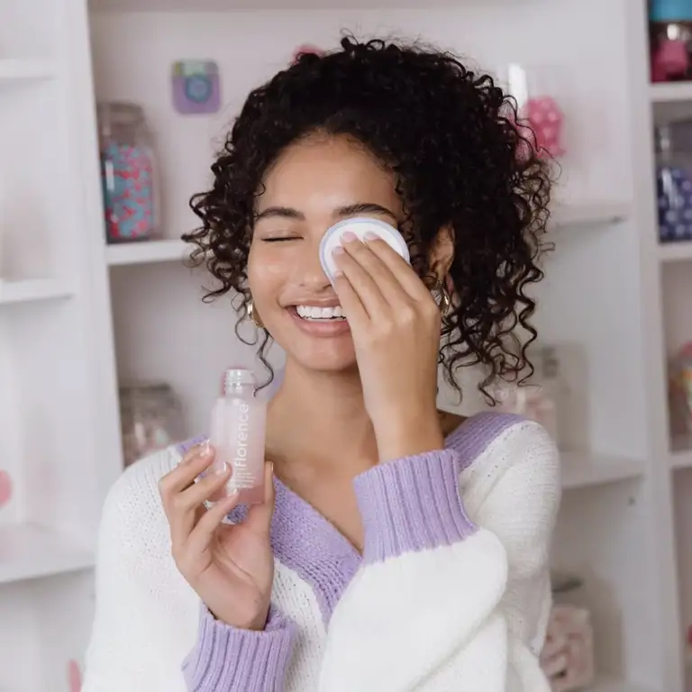 a woman is cleaning her face with a cotton pad while holding a bottle of lotion