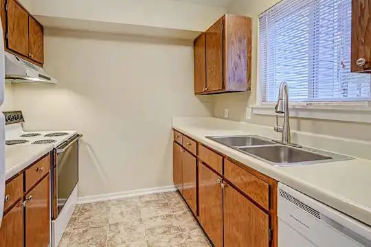 kitchen with natural light, dishwasher, electric range oven, extractor fan, light tile floors, light countertops, and brown cabinetry