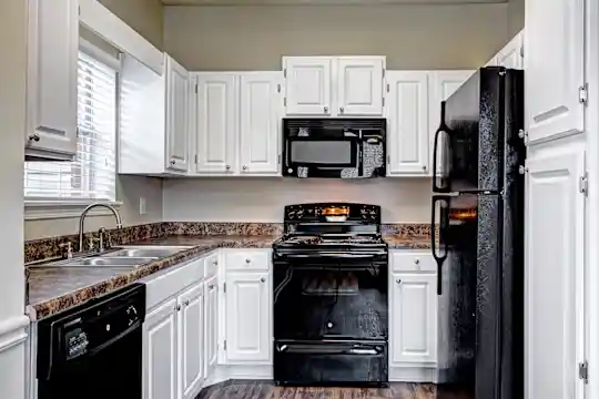 kitchen with natural light, refrigerator, electric range oven, dishwasher, microwave, dark stone countertops, white cabinetry, and dark floors