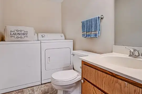 half bath with tile flooring, independent washer and dryer, mirror, toilet, and vanity