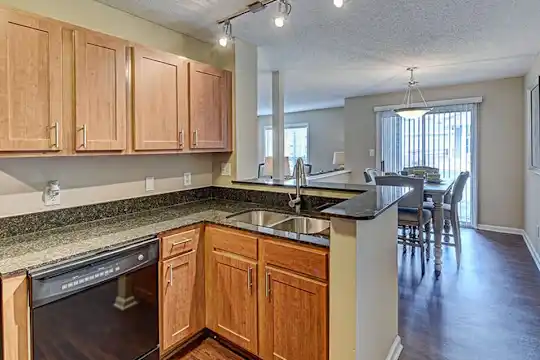 kitchen with natural light, dishwasher, dark floors, dark stone countertops, pendant lighting, and brown cabinetry