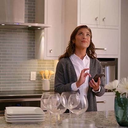 Woman standing in her kitchen using her smartphone to activate smart lighting in her home