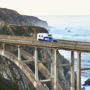 1970 Avion C11 truck camper crossing the Bixby Bridge in Big Sur with the ocean in the background.