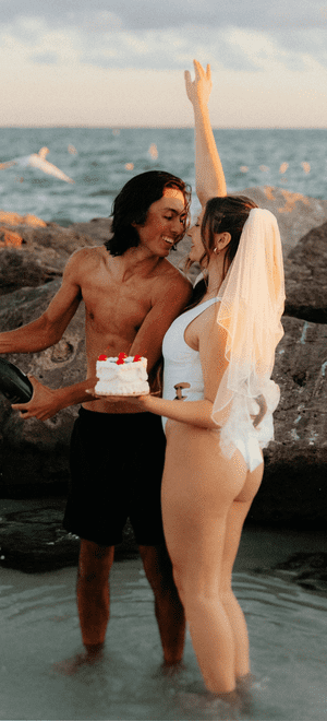 bride and groom on the beach for honeymoon holding a cake