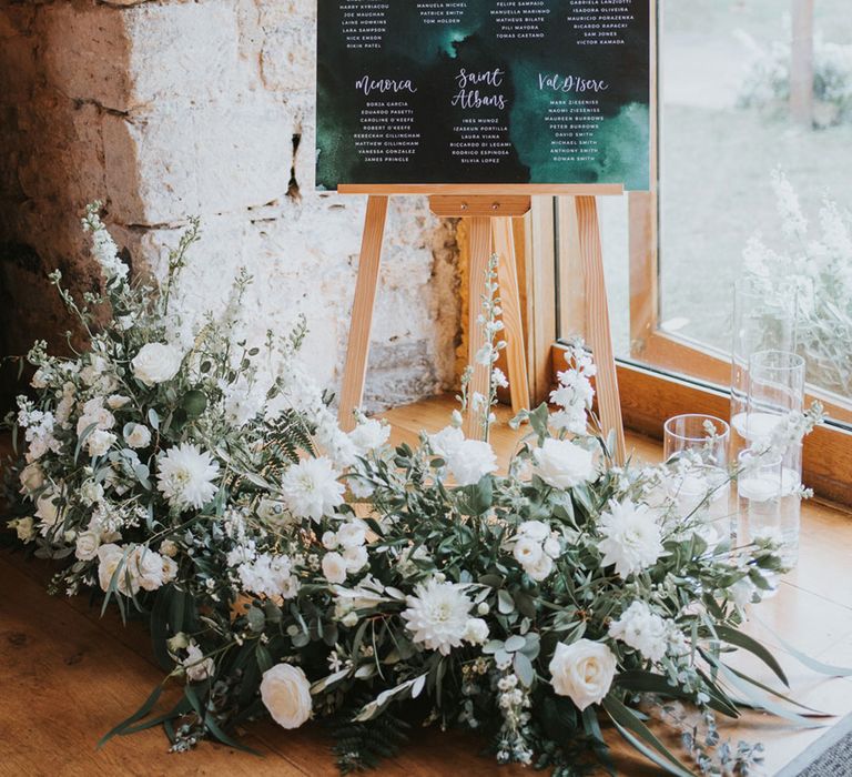 Dark green wedding table plan signage with white and green flowers with candle decorations 