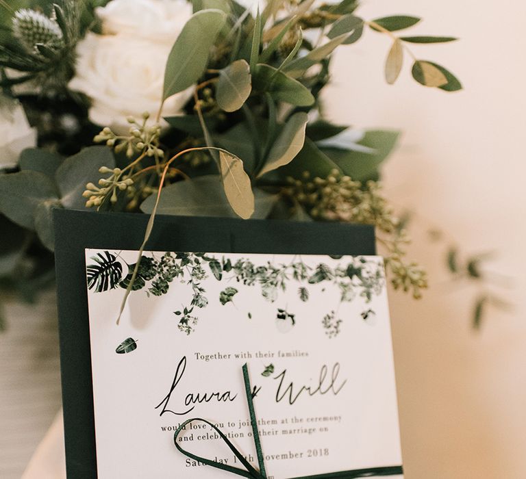 Green and white wedding stationery with leaf design tied to dark green envelope with green ribbon 