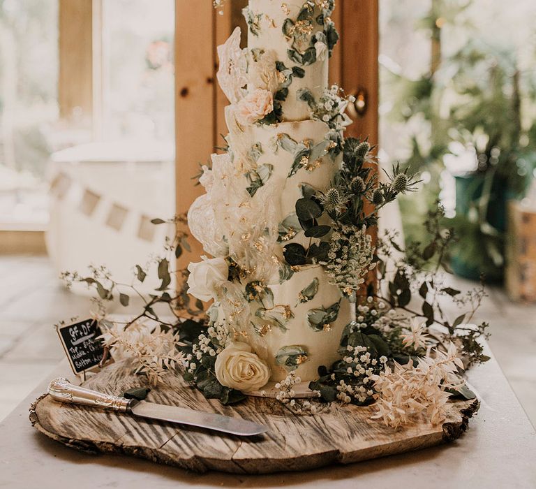 Three tier white frosted wedding cake with personalised gold cake topper with thistles, white roses, and gypsophila 