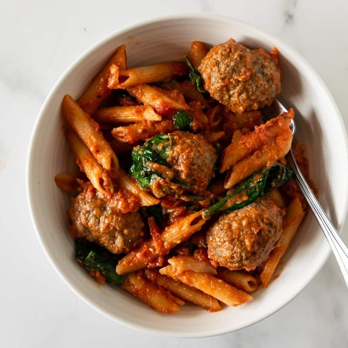 penne pasta with meatballs in a bowl with a fork.