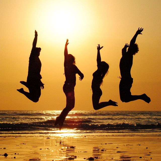 4 people jumping on the beach at sunset