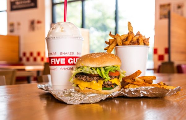 Photo of Five Guys - New York, NY, US. A Five Guys cheeseburger, milkshake and regular order of fries sits on a table inside a Five Guys restaurant.