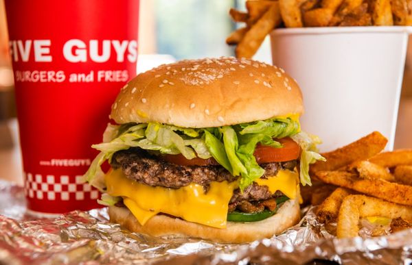 Photo of Five Guys - Philadelphia, PA, US. A close-up photograph of a Five Guys cheeseburger, soft drink in red Five Guys cup, and regular order of fries sitting on a t...