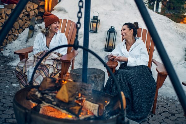 Photo of Nordik Spa-Nature Chelsea - Old Chelsea, QC, CA. A couple of friends visiting during the winter, sitting around a cozy fire for some laughs.