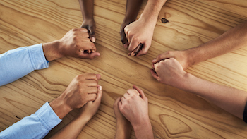 Diverse group holding hands around a table.