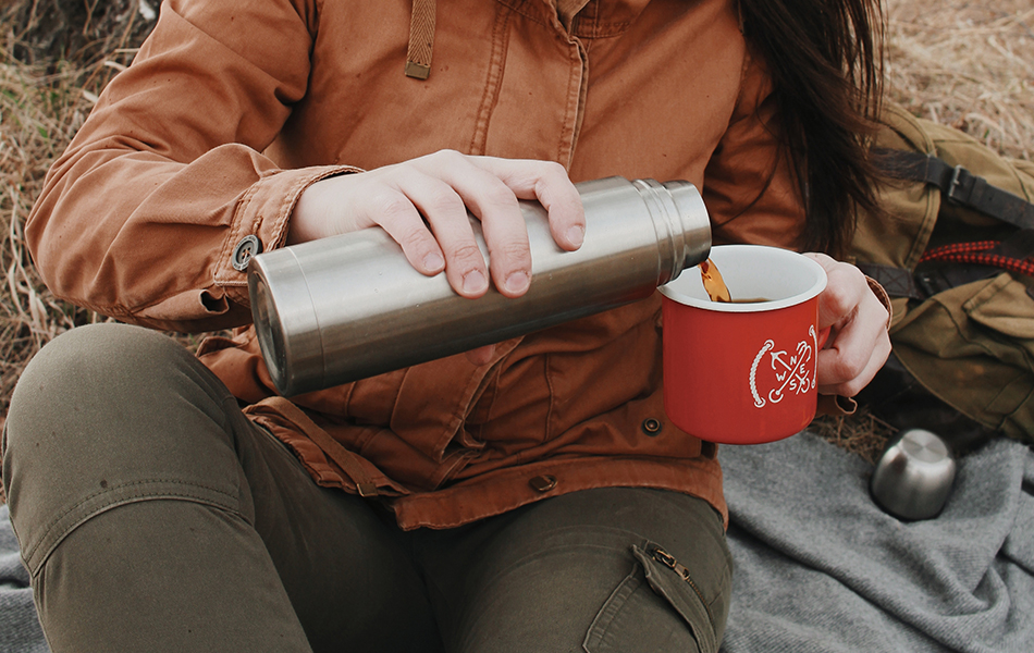 person holding a camping mug and a thermos