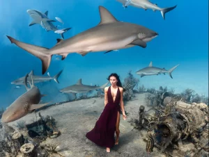 a woman walking underwater in a red dress among sharks